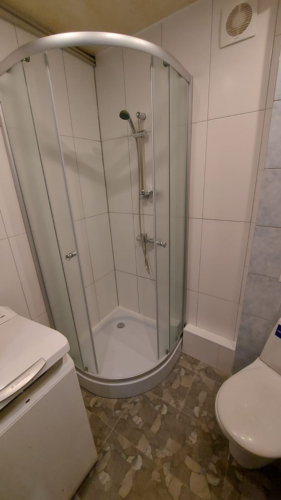 Jauna stūra duškabīne baltu flīžu vannas istabā